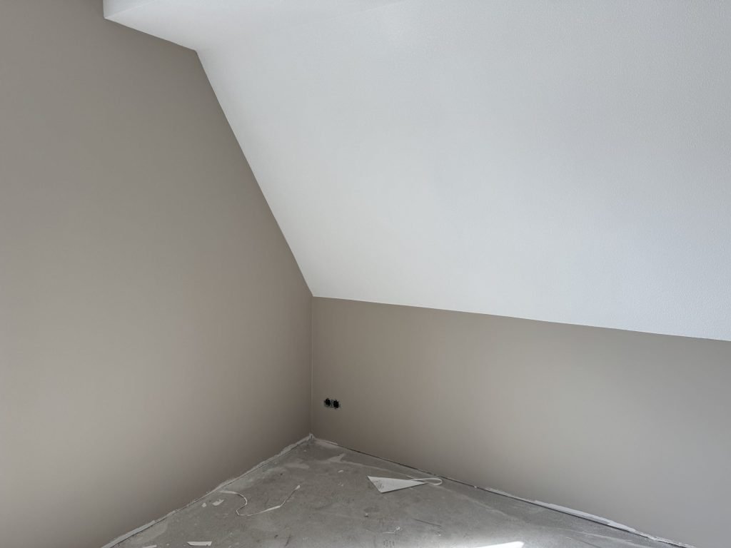 Zolderkamer met een schuine wand, een wit plafond en taupe geverfde muren, net afgewerkt