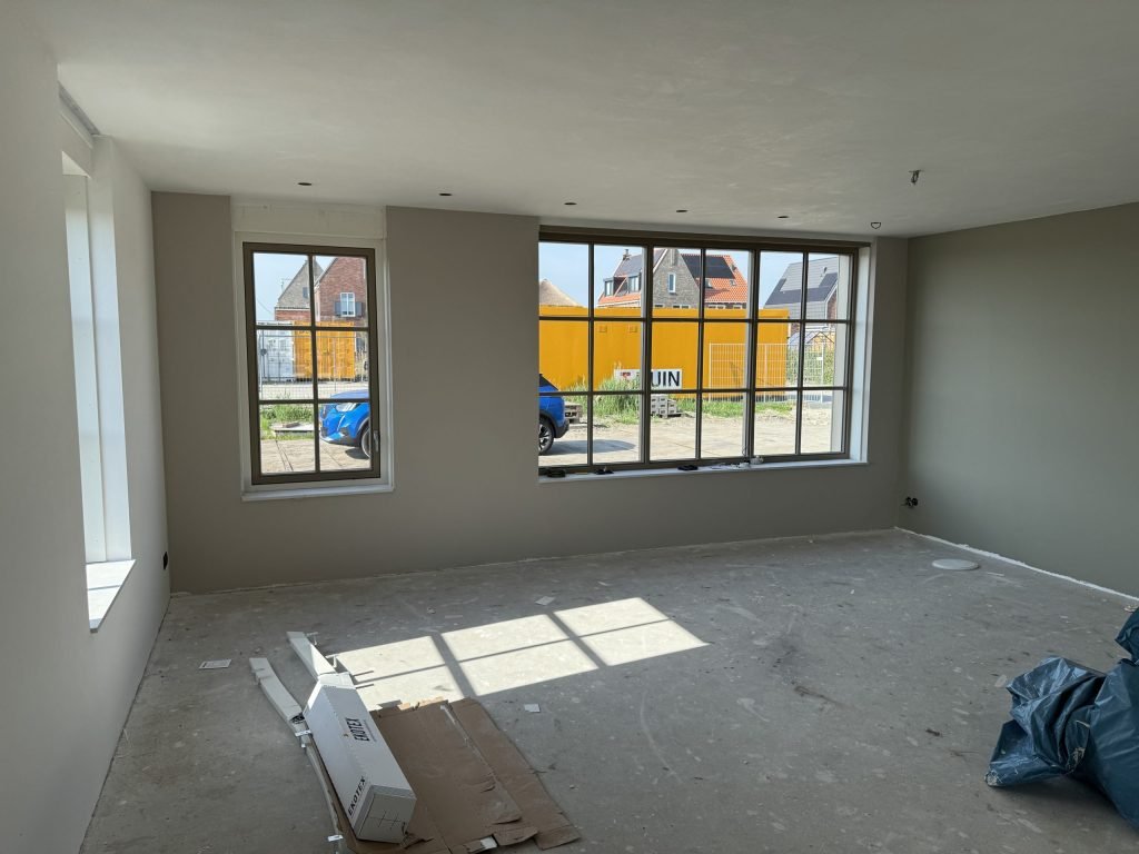 Woonkamer in aanbouw met grote roedenramen en wanden in een warme grijstint